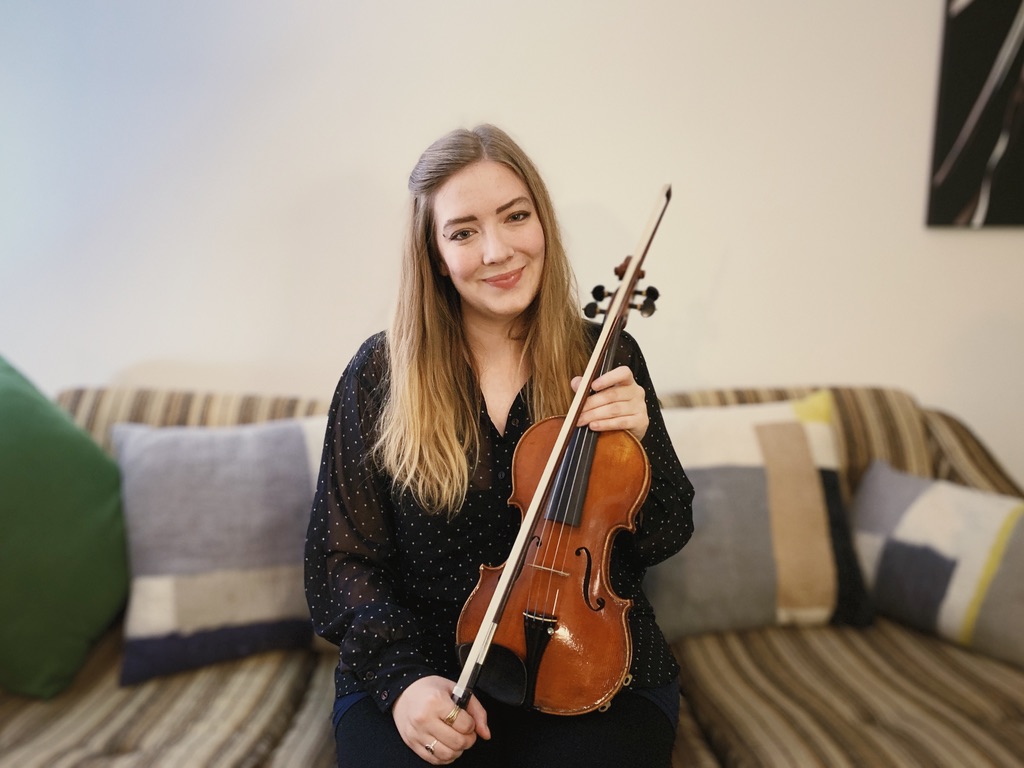Aline Homzy smiles at the camera while holding her violin and bow.